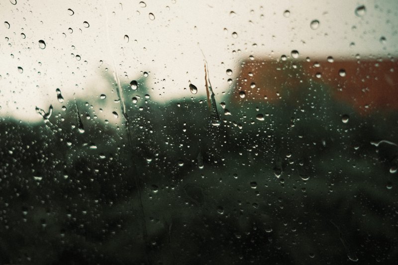 schlechte Tage: Regentropfen auf Fensterscheibe, ein Haus und Grün verschwommen dahinter