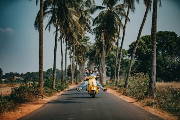 Paar fährt auf sonniger palmengesäumter Straße und reckt Beine und Köpfe hervor. Sie scheinen sich lebendig zu fühlen, so wie das ist, wenn man nach seinen Werten lebt