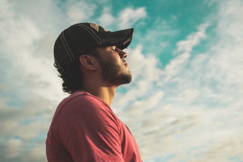 mentale Gesundheit: Mann mit schwarzer Kappe genißt den Moment der Sonne auf deinem Gesicht