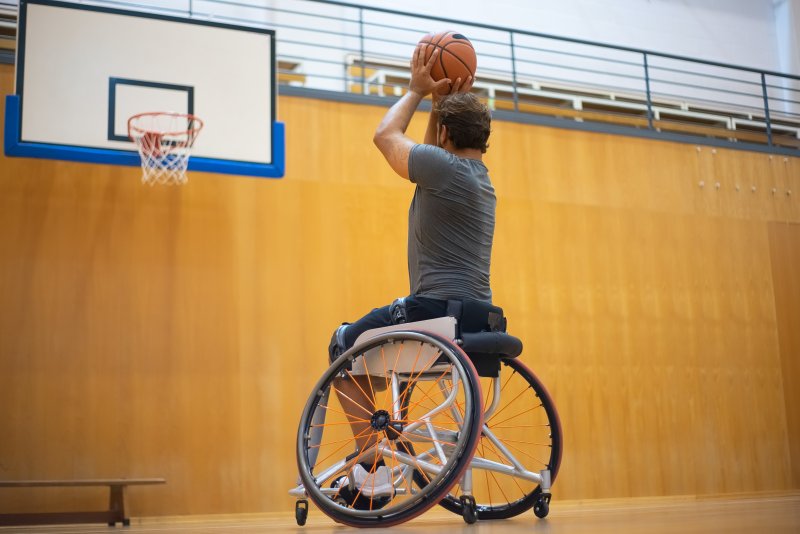 Ziele setzen: gehandicappter Sportler im Rollstuhl visiert mit Basketball den Korb an